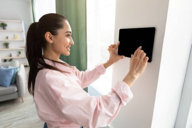 Oturma odasında akıllı duvar ev kontrol sistemi kullanan bir kadın