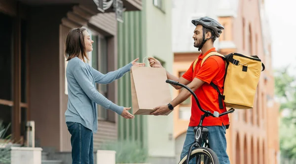 Smiling millennial indian male gives package to woman client near house