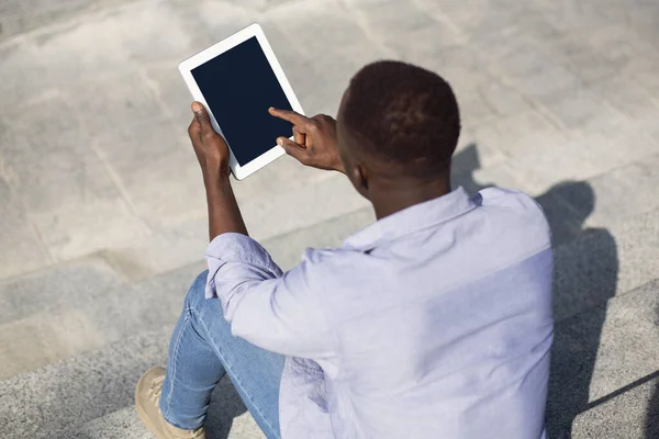 Jovem cara preto usando tablet computador com tela vazia em escadas de pedra ao ar livre, mockup para design do site — Fotografia de Stock