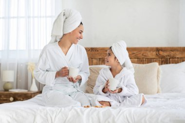 Sevimli anne ve kız yatakta çay içiyor.