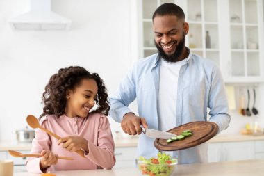 Neşeli afro baba ve kızı birlikte salata pişiriyorlar.