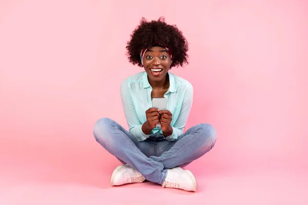 Excitado preto bushy senhora usando smartphone sentado sobre fundo rosa — Fotografia de Stock