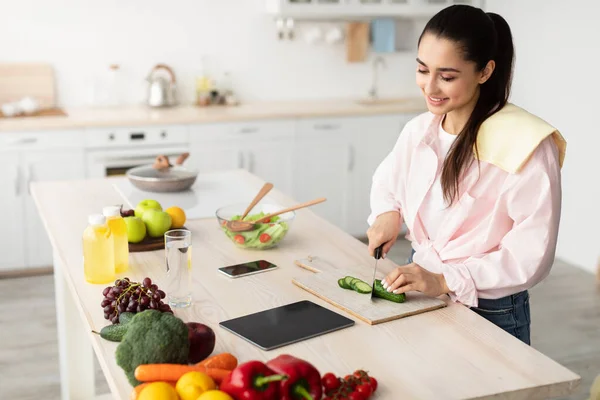 Kvinna matlagning sallad och använda tablett och kök — Stockfoto