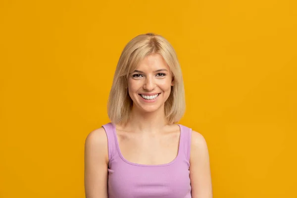 Gelukkig persoon. Portret van jonge vriendelijke vrouw met blond haar op zoek naar camera en glimlachen over gele achtergrond — Stockfoto