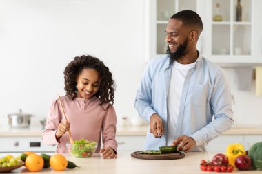 Afrikalı Amerikalı baba ve kız lezzetli taze salata pişiriyorlar.