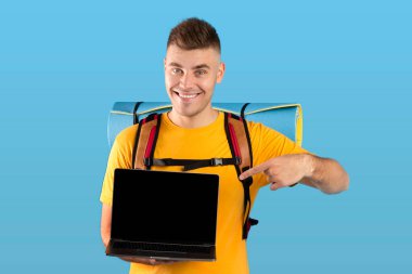 Mavi stüdyo arka planında boş ekranı olan dizüstü bilgisayarı gösteren olumlu milenyum adamı. Tasarım için model.