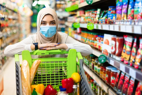 Muslim Woman In Mask Posing With Shop Cart In Supermarket