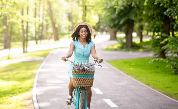 Radostná Afroameričanka v modrých šatech na kole v parku v létě — Stock fotografie