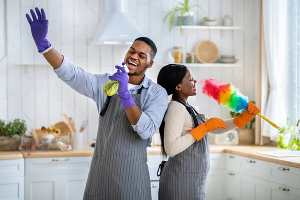 快乐的黑人夫妇在打扫厨房的家的时候，一边用清洁用品做哑剧一边唱歌 — 图库照片