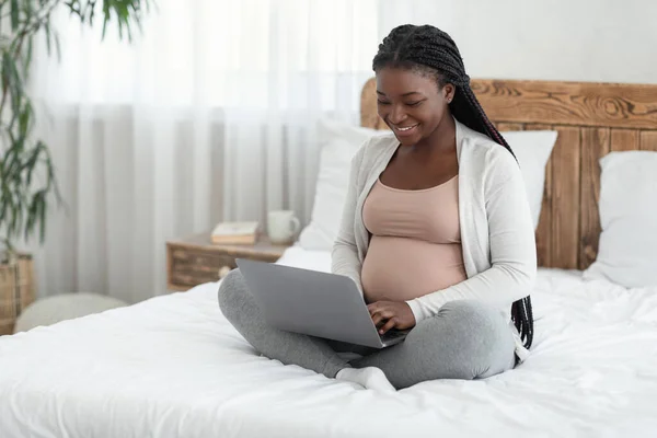 Online winkelen. Vrolijke zwarte verwachte moeder met behulp van laptop computer thuis — Stockfoto