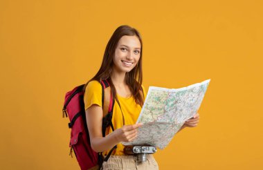 Sırt çantasıyla seyahat eden gülümseyen genç kadın, şehir haritasını tutuyor.