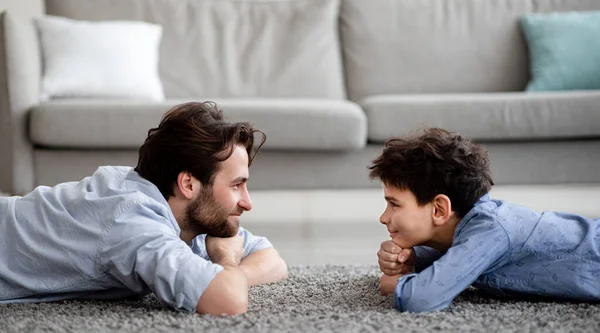 Feliz familia masculina. Perfil retrato del padre y su hijo acostados en la alfombra, mirándose y sonriendo — Foto de Stock