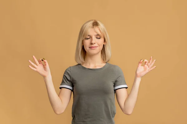 Ζεν. Ηρεμία γυναίκα διαλογίζεται πάνω από μπεζ φόντο στούντιο, κρατώντας τα χέρια σε χειρονομία mudra — Φωτογραφία Αρχείου