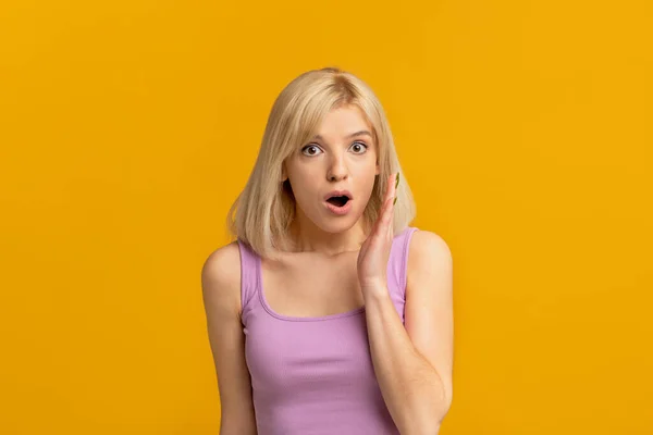 Megdöbbentő pletyka. Érzelmi szőke nő tartja a kezét közel nyitott száj mondja titok felett sárga stúdió háttér — Stock Fotó