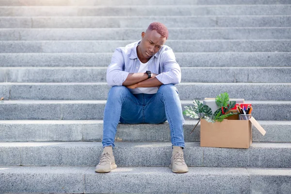 Bancarrota y desempleo. Tipo negro estresado con cosas personales sentirse molesto después de perder el trabajo en las escaleras fuera —  Fotos de Stock