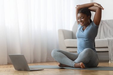 Ev sporu. Siyahi bir kadın online öğretmenleri izliyor ve oturma odasında eğitim görüyor.