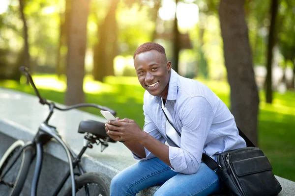 Homem negro feliz com bicicleta conversando no smartphone no parque urbano — Fotografia de Stock