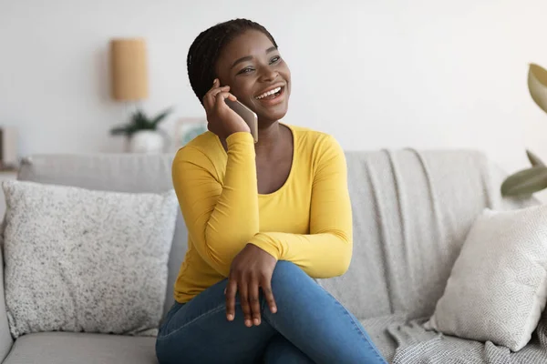 Positiva dama afroamericana hablando en el teléfono móvil en casa, disfrutando de la conversación —  Fotos de Stock