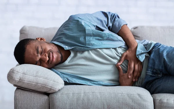 Africano ragazzo sofferenza da addominale dolore sdraiato su divano coperta — Foto Stock