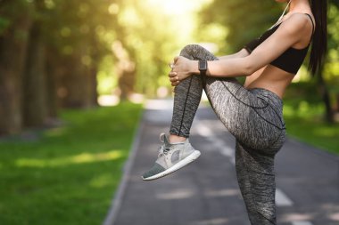 Kadın sporcu sabah koşusuna hazırlanıyor parkta koşuyor, bacak kaslarını esnetiyor.