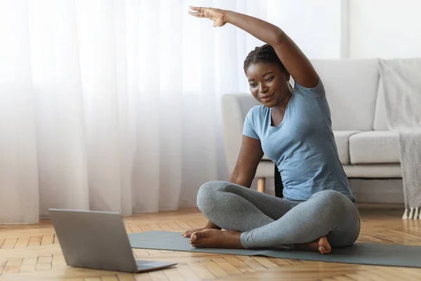 Онлайн фитнес. Улыбающаяся черная леди тренировки перед ноутбуком дома — стоковое фото