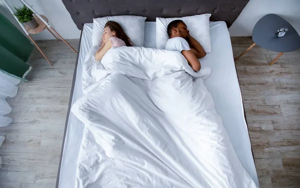Tysiącletnia para wielorasowa odwraca się od siebie, śpi w łóżku w domu, widok z góry — Zdjęcie stockowe