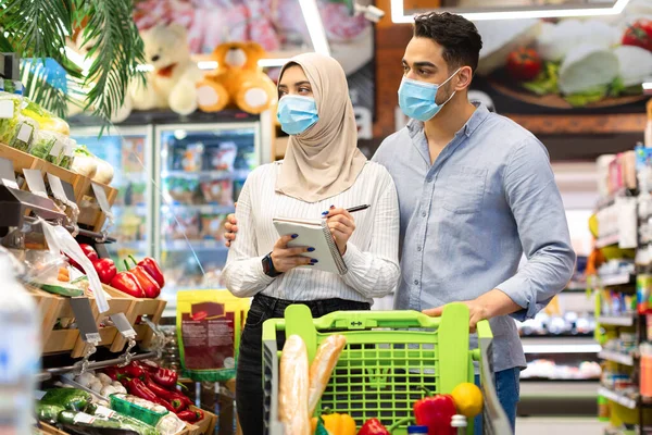 Μουσουλμάνοι σύζυγοι σημειώνοντας στη λίστα αγορών παντοπωλείων στο σούπερ μάρκετ — Φωτογραφία Αρχείου