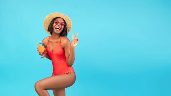 Bezstarostné černošky dáma v bikinách pití čerstvého letního koktejlu, ukazuje vítězství gesto na modrém pozadí, panorama — Stock fotografie