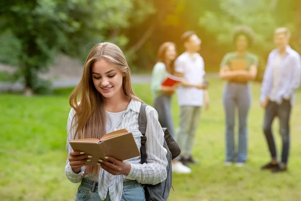 Concepto de aprendizaje. Estudiante bastante universitaria leyendo libro, preparándose para conferencias al aire libre — Foto de Stock