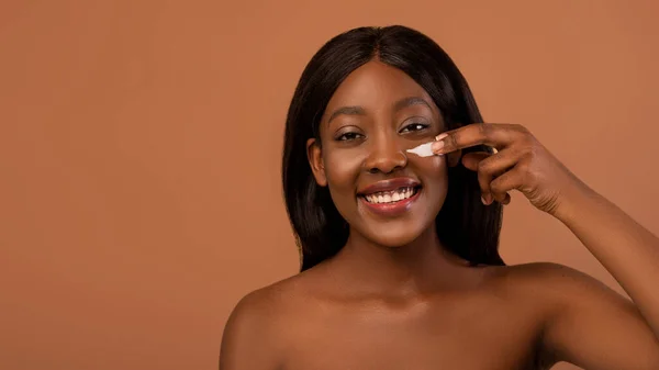 Sonriente mujer negra en topless con crema para los ojos —  Fotos de Stock