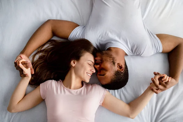 Vista dall'alto della giovane coppia multirazziale sdraiata sul letto, coccolandosi, esprimendo affetto l'uno per l'altro — Foto Stock