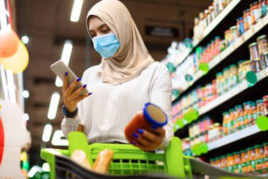 Marketten alışveriş yaparken akıllı telefon kullanan Müslüman kadın.