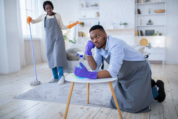 Millennial black man feeling exhausted from housework, his angry girlfriend scolding him for being lazy, free space