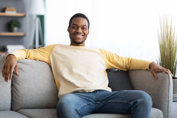 Feliz hombre negro sentado en el sofá en casa —  Fotos de Stock