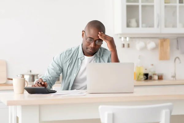Hombre negro maduro estresado usando calculadora y computadora portátil, calculando impuestos, comprobando gastos mensuales — Foto de Stock