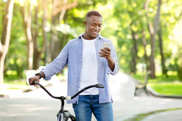 Legal afro americano cara com moderno bicicleta envio mensagem no celular no parque — Fotografia de Stock