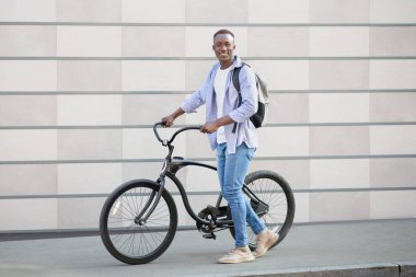 Sırt çantası ve modern bisikleti olan yakışıklı siyahi adam. Şehir caddesinde tuğla duvarın yanında.