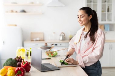 Kadın salata pişiriyor, dizüstü bilgisayar ve mutfak kullanıyor.
