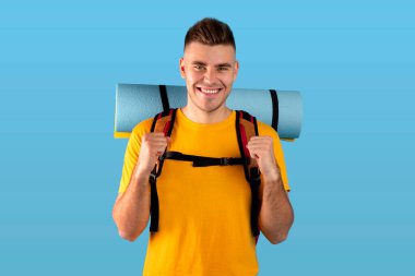 Turist vitesli neşeli genç adam mavi stüdyo geçmişi üzerinden EVET işareti yapıyor.