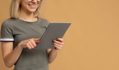 En yeni dijital tabletle tanınmayan genç bir kadın bej renkli stüdyo arka planında boş bir alanda duruyor.