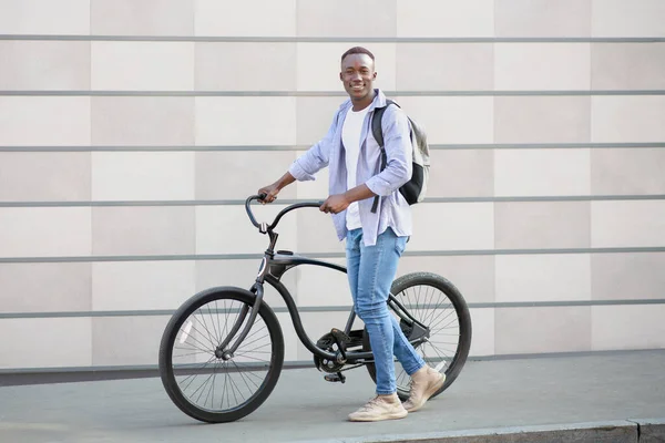 Fešák černošky chlap s batohem a moderní kolo v blízkosti cihlové zdi na ulici — Stock fotografie