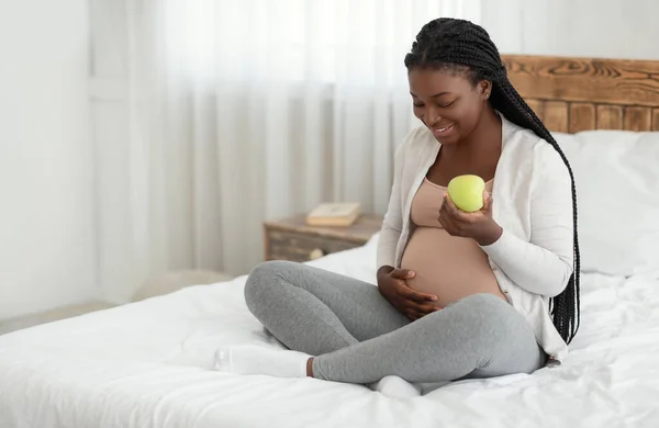 Dieta de Gravidez Saudável. Mulher africana grávida comendo maçã enquanto descansa na cama — Fotografia de Stock