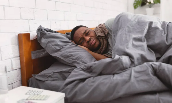 Ongelukkig ziek zwart guy liggend verpakt in deken in slaapkamer — Stockfoto