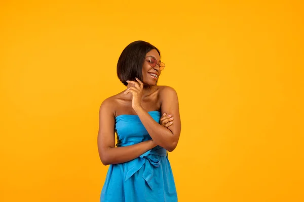 Yaz modası. Güzel mavi elbiseli, güneş gözlüklü, turuncu stüdyo arka planında poz veren ve gülümseyen güzel siyahi kadın. — Stok fotoğraf