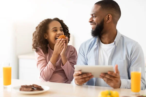 Ayah dan anak kulit hitam makan permen menggunakan tablet. — Stok Foto