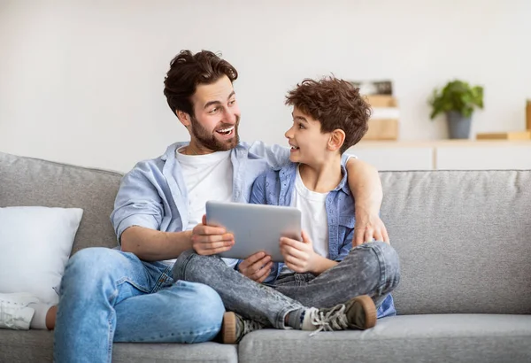 Familieweekend. Uitgesproken vader en zoon met behulp van tablet computer, surfen op internet terwijl het doorbrengen van tijd samen thuis — Stockfoto