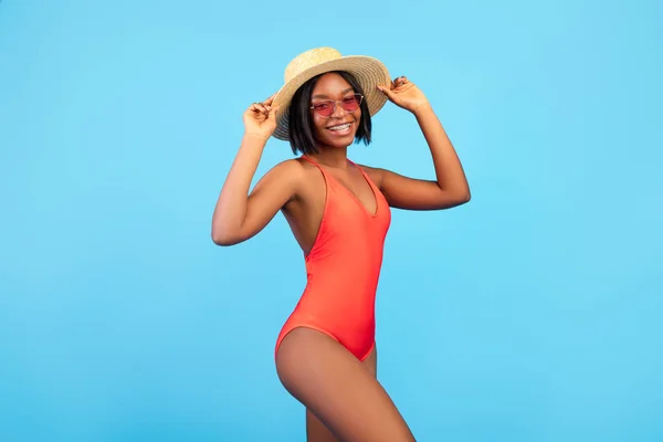Портрет веселої афроамериканської жінки в сексуальному купальнику, в солом'яному капелюсі і сонцезахисних окулярах на синьому тлі. — стокове фото