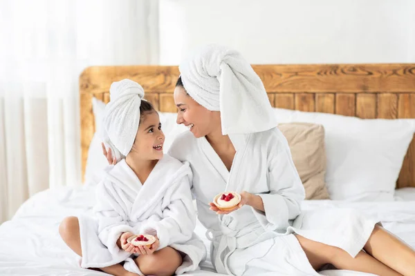 Mamma e bambino felici indossando accappatoi, mangiare pasticceria — Foto Stock