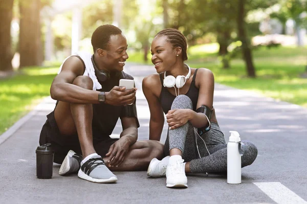 Χαμογελώντας μαύρο σπορ ζευγάρι αναπαύεται με Smartphone μετά την προπόνηση γυμναστικής — Φωτογραφία Αρχείου