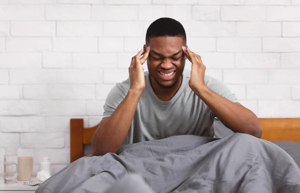 Hombre africano que sufre de dolor de cabeza Masajeando templos sentado en el dormitorio — Foto de Stock